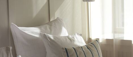 A neatly made bed with white bedding and striped pillows, a white headboard, and a hanging light fixture.