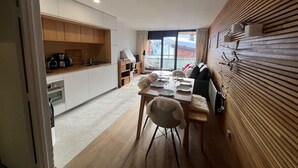 A modern kitchen with white cabinets, a dining area with a wooden table and chairs, and a cozy seating area with a sofa and cushions.