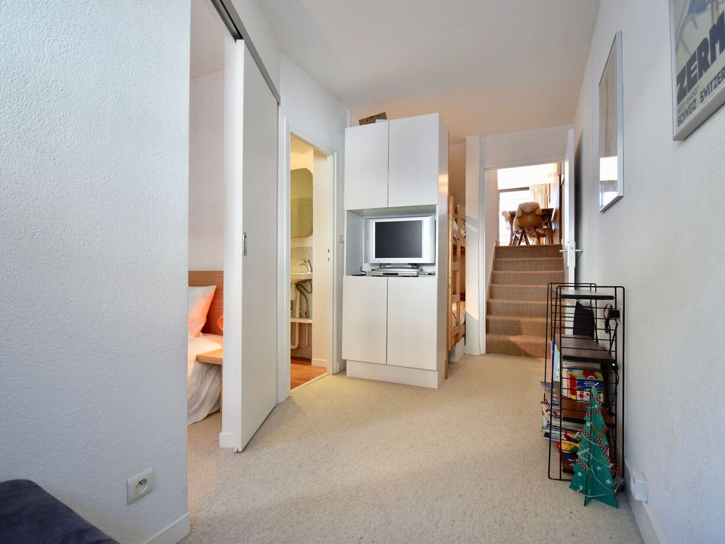A compact living space with a kitchenette, a television, a staircase, and a small Christmas tree.