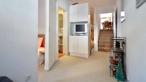 A compact living space with a kitchenette, a television, a staircase, and a small Christmas tree.