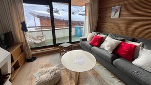 A modern living room with a grey sofa, a round white coffee table, and a large window with a view of a snowy landscape.
