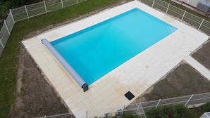 A rectangular swimming pool with a tiled deck, surrounded by a metal fence, and adjacent to a road.