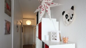 A hallway with a staircase, a white cabinet with red drawers, a panda mask, and a paper crane decoration.
