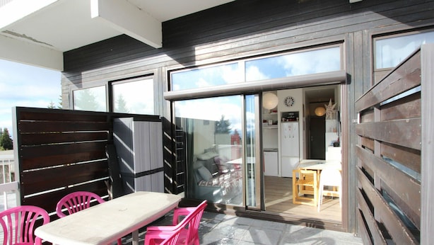 A patio with a table and chairs, a sliding glass door leading to a kitchen, and a wooden fence.
