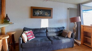 Un salon avec un canapé bleu foncé, une table basse en bois, une lampe et un tableau accroché au mur.