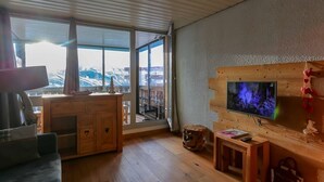 Un salon moderne doté d’un grand téléviseur, de meubles en bois et offrant une vue sur les montagnes grâce à de grandes fenêtres.