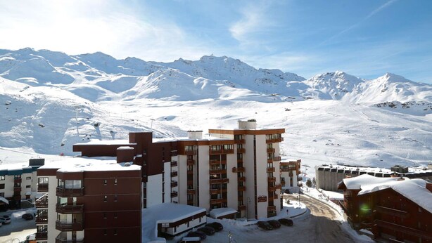Un paysage montagneux enneigé, avec un hôtel doté de plusieurs étages et de balcons, se dressant sur fond de pics enneigés.
