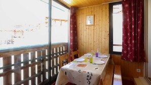 Ein Essbereich mit Tisch für zwei Personen, Holzwänden und großen Fenstern mit Vorhängen.