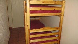 Ein hölzernes Etagenbett mit drei Schlafstellen, jede mit einer rot karierten Matratze.