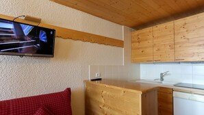 Eine kleine Küche mit Holdekor-Schränken, einer eingebauten Spüle und einem an der Wand befestigten Fernseher.