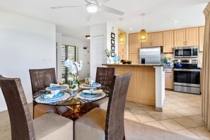 A modern kitchen with wooden cabinets, stainless steel appliances, and a dining area with a glass table and chairs.
