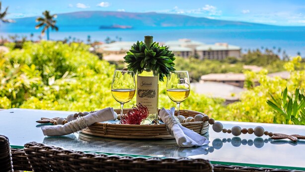 A table with a bottle of wine, two glasses, and a decorative centerpiece. - Tropical Escape with Endless Coastal Views (Kihei)