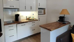 A compact kitchenette with white cabinets, a microwave, a coffee machine, and a small table with a lamp. - 2-Bedroom Apartment with Parking, Sleeps 4/6 (Cauterets)
