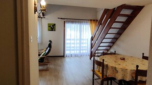A dining area with a table and chairs, a wooden bench, a staircase, and a window with curtains. - 2-Bedroom Apartment with Parking, Sleeps 4/6 (Cauterets)