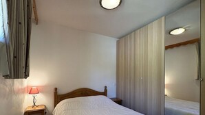 A bedroom with a wooden bed, a bedside table with a lamp, a wardrobe, and a mirror. - Cozy Ski-In/Ski-Out Apartment with Pool & Sauna, Sleeps 6 (Les Orres)