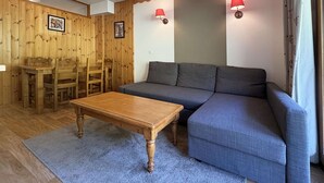 A room with a wooden dining table and chairs, a sofa, and two wall-mounted lamps. - Cozy Ski-In/Ski-Out Apartment with Pool & Sauna, Sleeps 6 (Les Orres)
