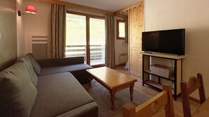 A furnished room with a sofa, a coffee table, a TV on a stand, and a sliding glass door leading to an outdoor area. - Cozy Ski-In/Ski-Out Apartment with Pool & Sauna, Sleeps 6 (Les Orres)
