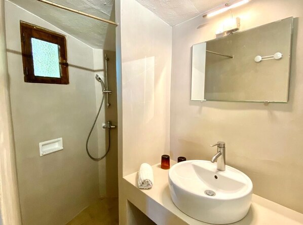 Een badkamer met een douchecabine van glas, een witte wastafel, een spiegel en een handdoek op het aanrecht.