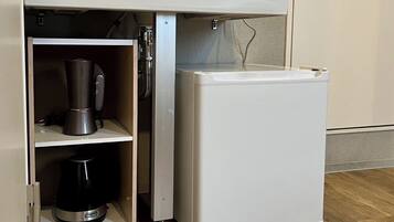 Una cocina compacta con refrigerador incorporado y un estante con cafetera y hervidor.