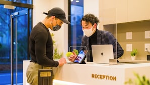 Una reception con una scrivania, un laptop, un tablet, un cartello con la scritta 'RECEPTION' e una porta in vetro che dà sull'esterno.