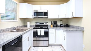 A compact kitchen with white cabinets, a stainless steel stove, a microwave, and a dishwasher.