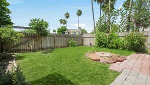 A backyard with a wooden fence, a brick patio, and a small garden area with red flowers.