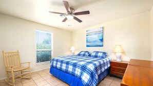 A bedroom with a bed, a rocking chair, a nightstand, a lamp, and a ceiling fan.