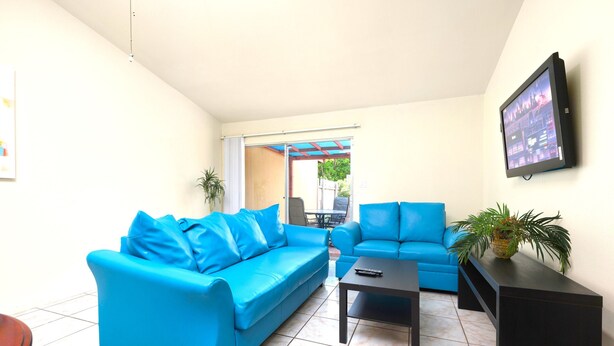 A living room with two blue sofas, a black coffee table, and a TV mounted on the wall.