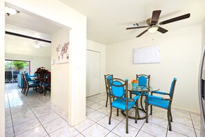 Uma sala de jantar com uma mesa, cadeiras, ventilador de teto e piso ladrilhado.