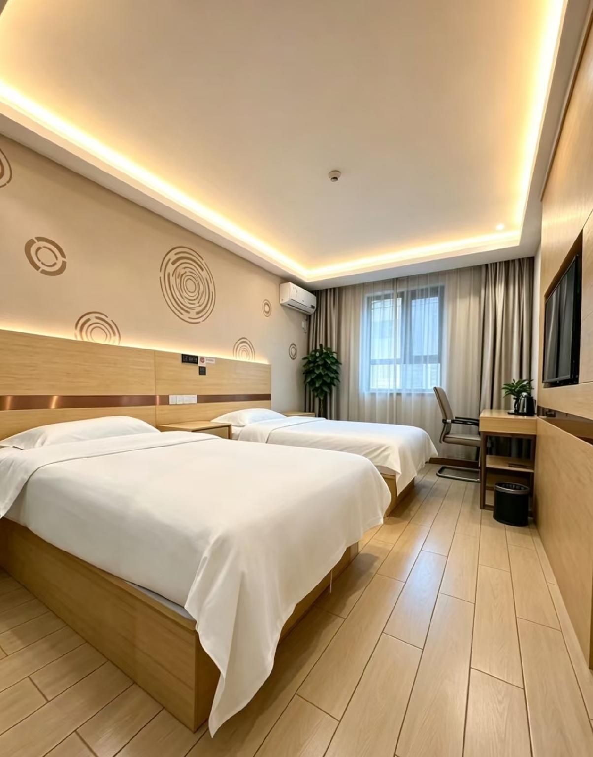 A hotel room with two beds, a desk, a chair, a TV, and a potted plant.