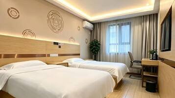 A hotel room with two beds, a desk, a chair, a TV, and a potted plant.