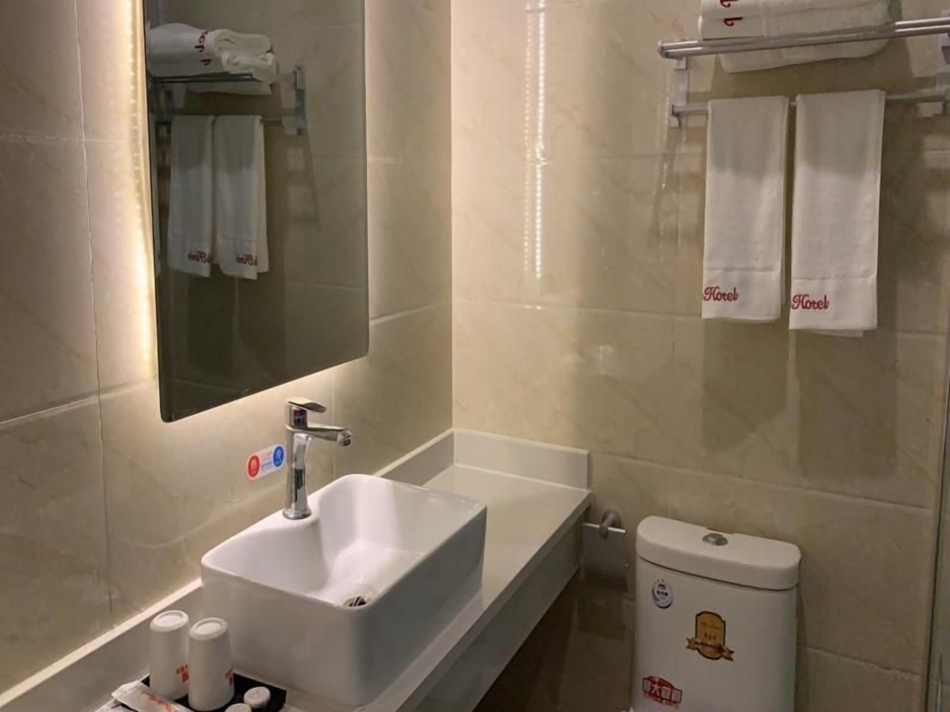 A bathroom with a sink, mirror, and toilet. There are towels hanging on a rack and a sign indicating no smoking.