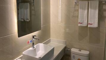 A bathroom with a sink, mirror, and toilet. There are towels hanging on a rack and a sign indicating no smoking.