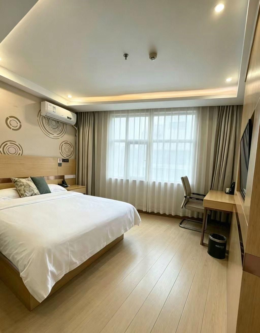 A hotel room with a bed, a desk, a chair, a TV, and a window with curtains.