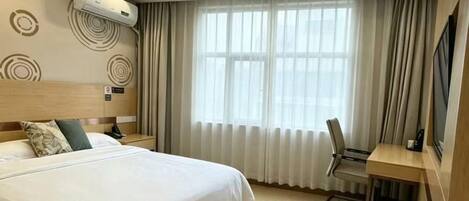 A hotel room with a bed, a desk, a chair, a TV, and a window with curtains.