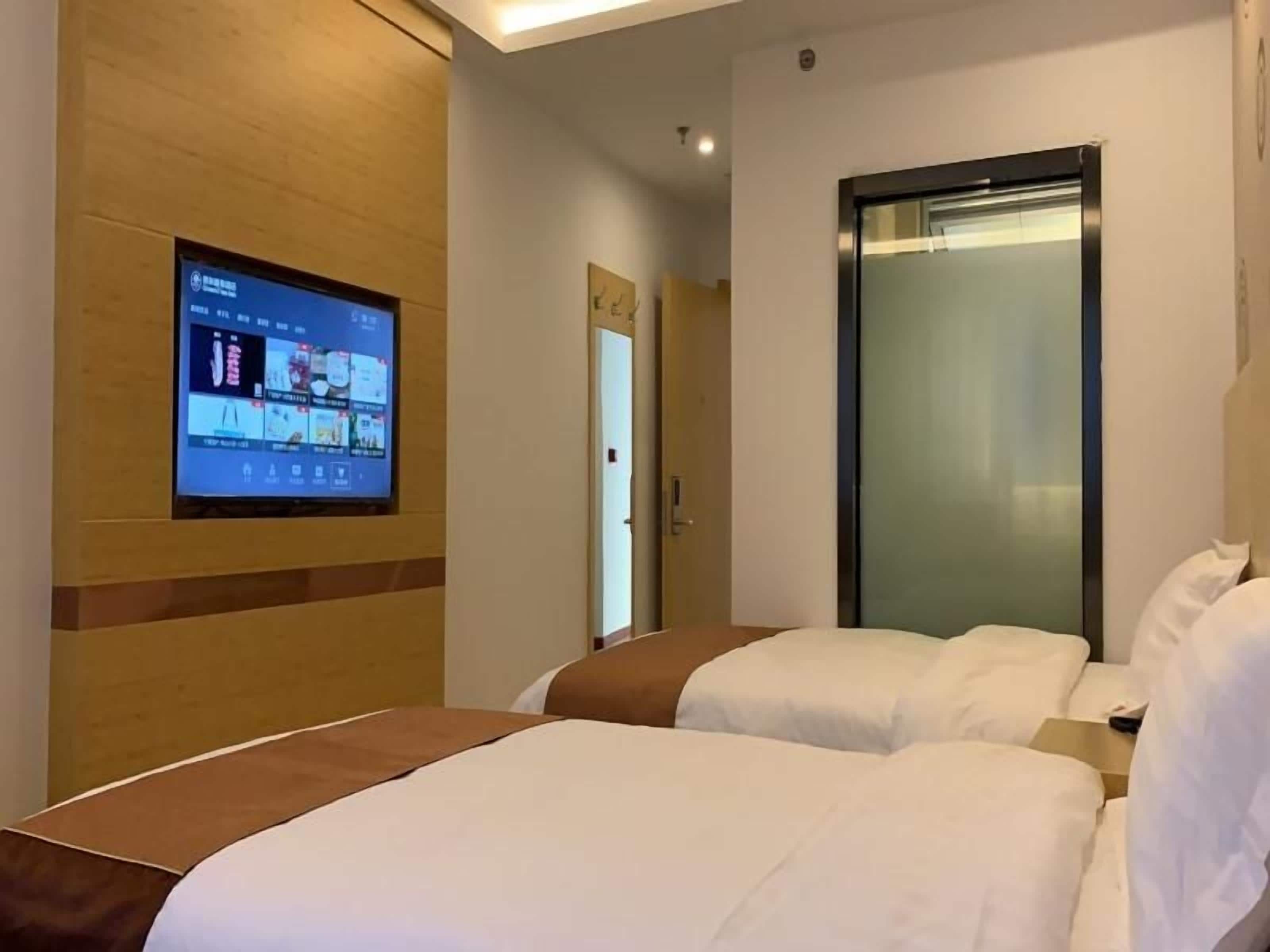 A hotel room with two beds, a TV mounted on the wall, and a door leading to a hallway.