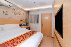 Quarto de hotel com cama, televisão, porta de madeira e parede com padrões circulares.