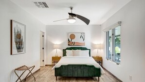 Ein Schlafzimmer mit einem Bett, zwei Nachttischen, einem Deckenventilator, einem Fenster und Bildern an den Wänden.