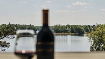 A bottle and glass of wine in the foreground with a lake and trees in the background.