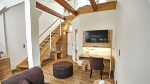 A modern living room with a staircase, wooden flooring, a flat-screen TV, a sofa, a coffee table, and a desk. - Loungehotel Seeterrassen Wandlitzsee (Wandlitz)