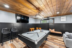 A pool table in a room with a wooden ceiling, black and orange chairs, and a television mounted on the wall. - Luxury 3 BR w/ Hot Tub, Fire Pit, Outdoor Kitchen, Gazebo (Gatlinburg)