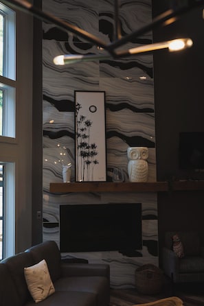 A modern living room with a large wall-mounted TV, a fireplace, and a framed artwork above it. - Luxury 3 BR w/ Hot Tub, Fire Pit, Outdoor Kitchen, Gazebo (Gatlinburg)