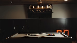 A pool table with balls and cues, a chair, and a small orange stool.