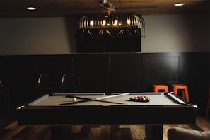 Une table de billard avec des billes et des queues, une chaise et un petit tabouret orange.