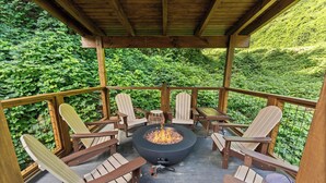 A wooden deck with Adirondack chairs and a central fire pit.