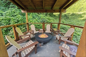 Une terrasse en bois avec des fauteuils Adirondack et un foyer central.