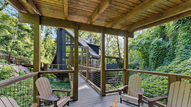 Un terrazza in legno con poltrone Adirondack e un braciere, con vista su una zona boschiva.
