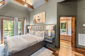 Une chambre à coucher avec un grand lit, des lampes de chevet, une tête de lit et une vue sur l’extérieur par une fenêtre.
