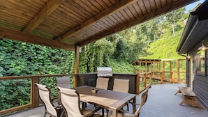 Una terrazza esterna con tavolo e sedie di legno, un barbecue e vista su una zona boschiva.