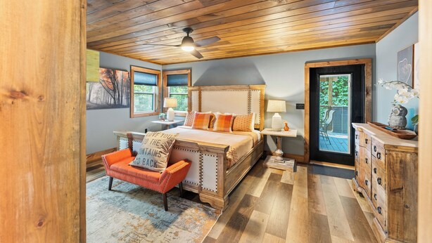 A bedroom with a wooden ceiling, a bed with multiple pillows, a nightstand, a chair, and a dresser.